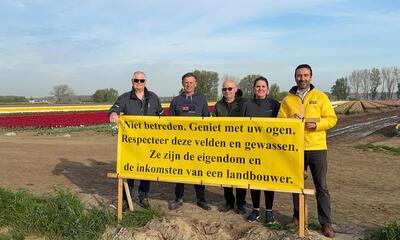 Koen Daniëls en bestuursleden met spandoek bij tulpenveld in Meerdonk